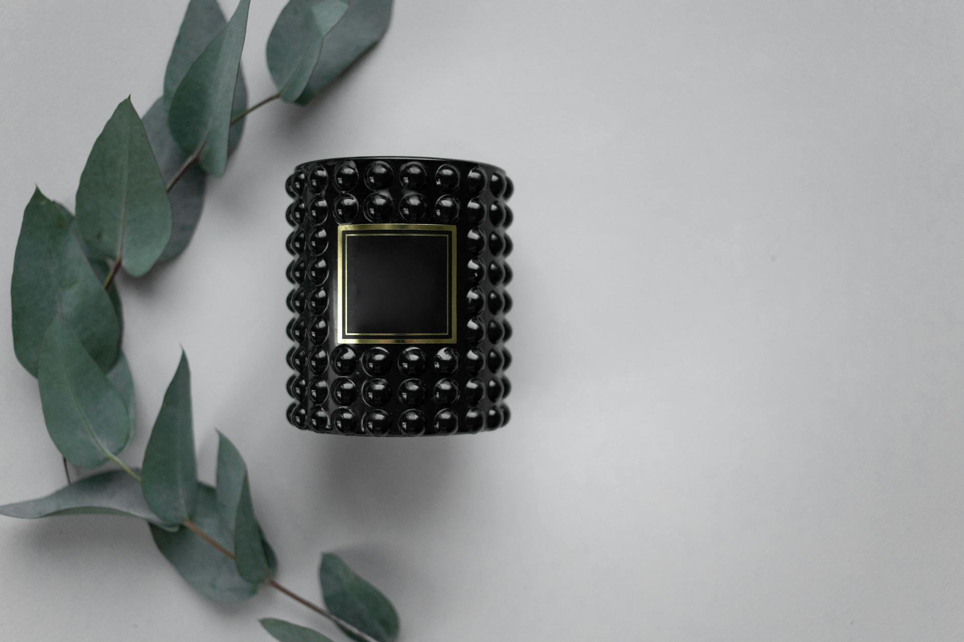 Czarny świecznik o fakturowanej powierzchni z gałązką eukaliptusa na szarym tle