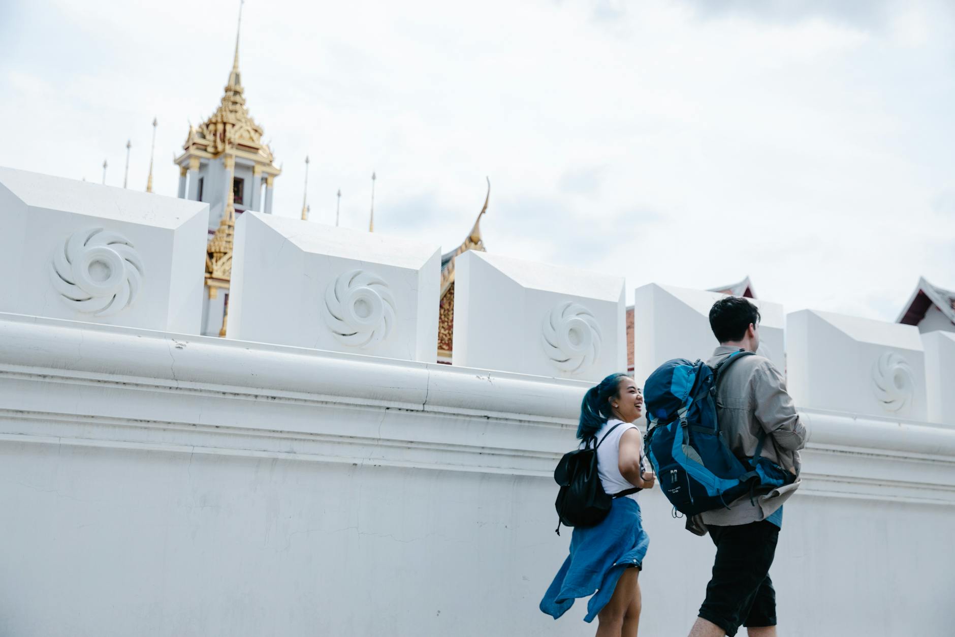 Dwóch turystów idzie wzdłuż białego muru w Bangkoku, w tle złota wieża świątyni
