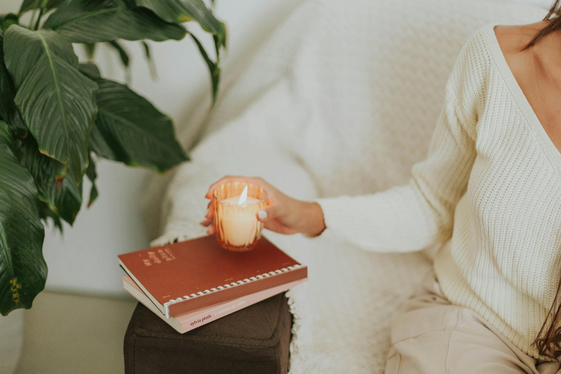 Kobieta w mieszkaniu trzyma zapaloną świecę obok książek i rośliny