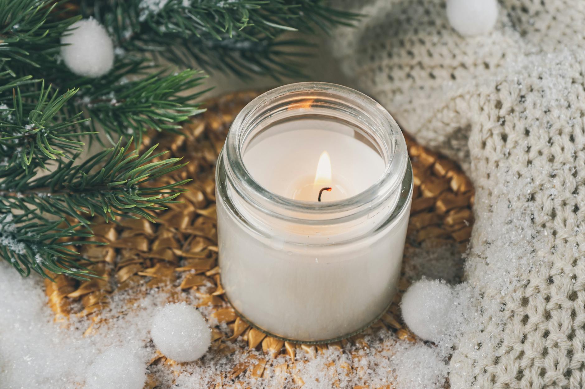 Zimowa świeca sojowa wśród śniegu i gałązek sosny