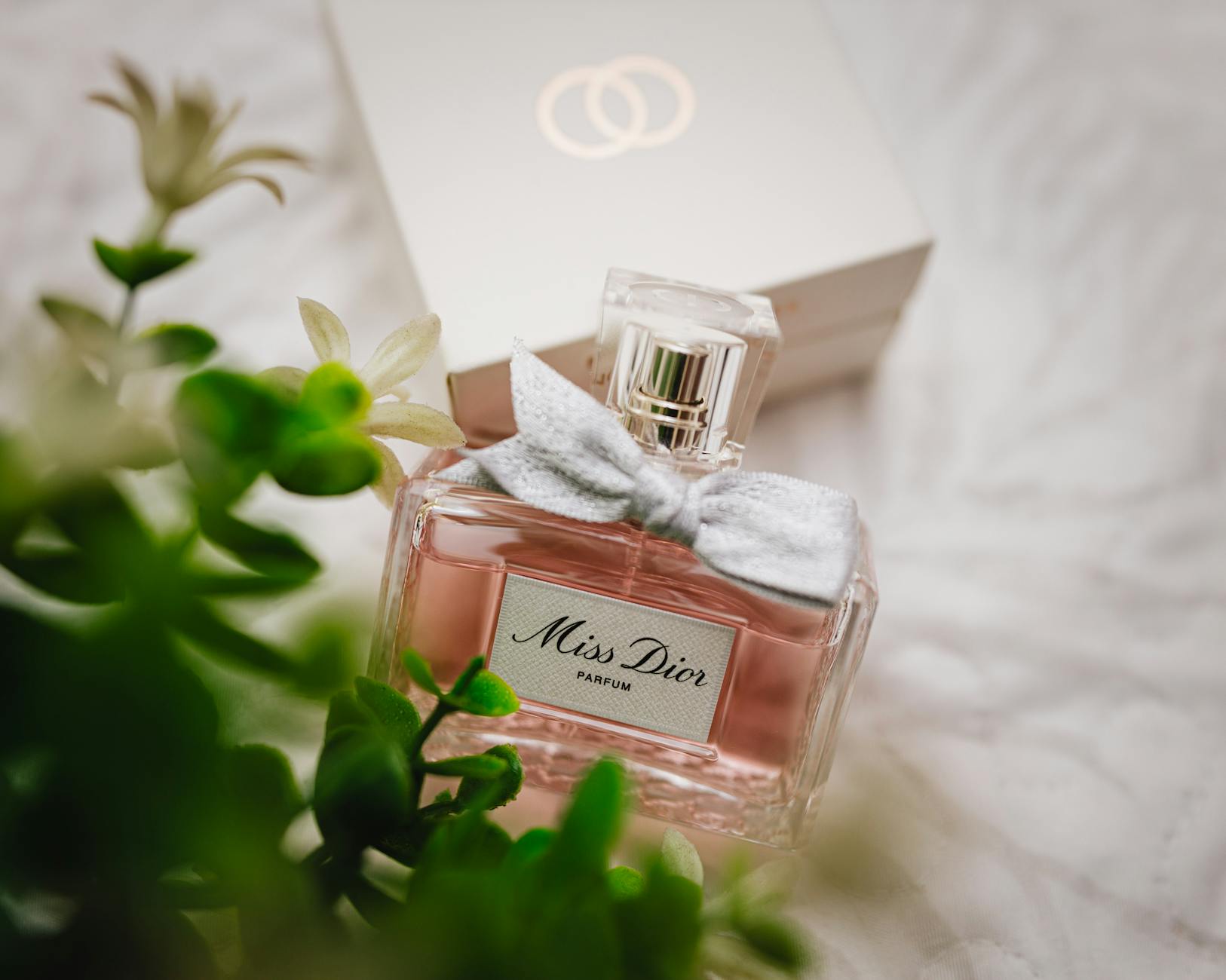 Flakon perfum Miss Dior na tle rozmytych, jasnych kwiatów