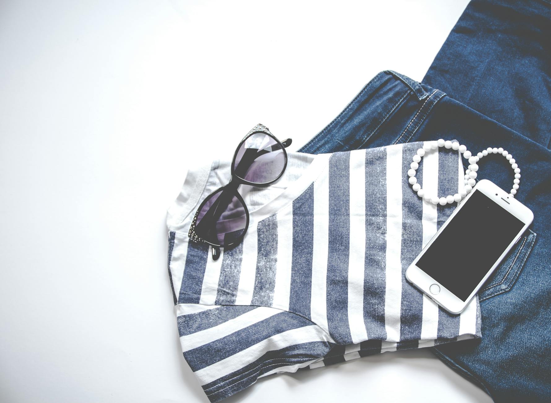 Minimalistyczny flat lay: okulary, pasiasta bluzka, jeansy i smartfon