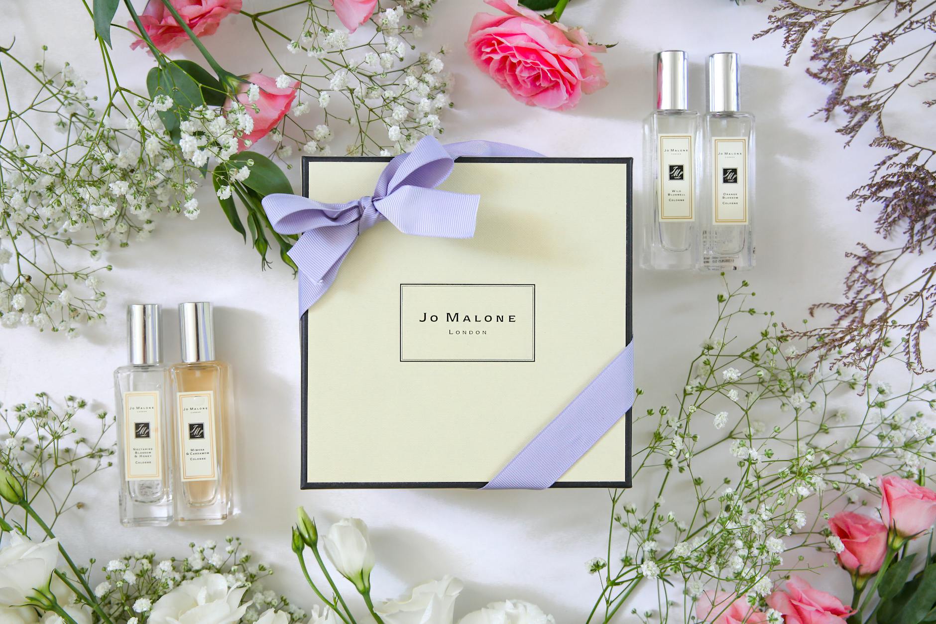 Perfumy Jo Malone wśród różowych róż i delikatnych białych kwiatów