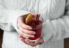 Świeca o zapachu grzanego wina (Mulled Wine): jak dobrać odpowiednią intensywność do metrażu pokoju? Dłonie w swetrze trzymają kubek grzanego wina z cytrusami i przyprawami